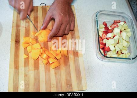 Koch schneidet Mango auf Holzoberfläche. Schneiden Sie frische Mango in Würfel für die Zubereitung von Smoothies Stockfoto