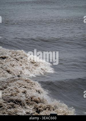 QIANJIANG-Tidalbohrung. Schlammige Meereswellen stürzen heftig gegen das Ufer und erzeugen einen Spritzer braunem Schaum und Wasser. Stockfoto
