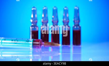 Spritze und Durchstechflaschen werden während einer Laboreinstellung auf einem Tisch mit blauem Hintergrund angezeigt Stockfoto