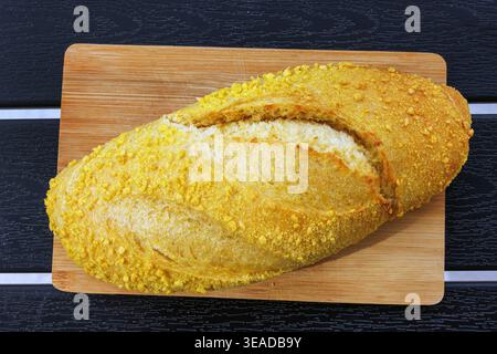 Blick von oben auf einen kroatischen Maisbrotlaib, der auf einem Holzschneidebrett auf einem dunklen Lattentisch steht. Selektiver Fokus Stockfoto