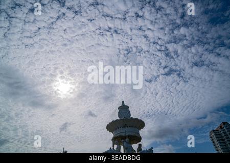 Phuket Thailand. 13. August 2025: Eine markante weiße Skulptur steht hoch unter einem strukturierten, bewölkten Himmel, deren anmutige Form sich mit dem flauschigen c kontrastiert Stockfoto
