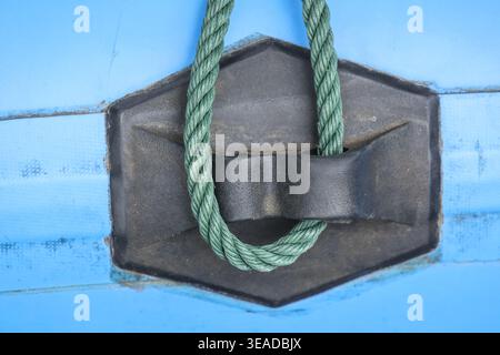 Nahaufnahme des grünen Seils, das fest mit der schwarzen Metallklammer auf blauer Oberfläche verbunden ist, zeigt eine starke Verbindung und Stabilität in nautischer Umgebung, die e fördert Stockfoto