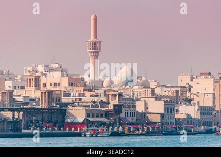 12. Januar 2026, Dubai, VAE: Blick auf das Ufer des Creek mit traditionellen Gebäuden, Moschee-Minarett und Booten, die arabisches Erbe widerspiegeln Stockfoto