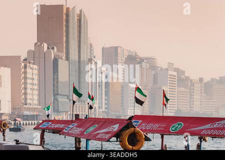 12. Januar 2026, Dubai, VAE: Abra Water Taxi Terminal am Creek mit Blick auf die Skyline von Deira mit den VAE-Flaggen im Vordergrund Stockfoto