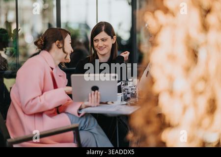 Zwei weibliche Kollegen, die ein Geschäftstreffen in einem Café halten, während sie ein Tablet teilen und lächeln Stockfoto