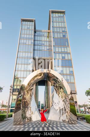 12. Januar 2026, Dubai, VAE: Frau in rotem Kleid lächelt unter dem Tor und symbolisiert moderne Architektur und Geschäftserfolg im Design Distric Stockfoto