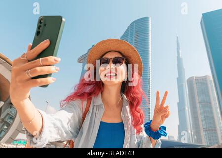 11. Januar 2026, Dubai, VAE: Frau macht ein Reiseselfie in Dubai, lächelt in die Smartphone-Kamera und zeigt ein Friedenszeichen Stockfoto