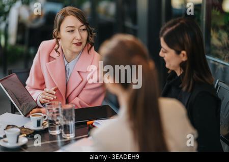 Drei Geschäftsfrauen diskutieren bei einem Treffen im Freien über Kaffee und Dokumente Stockfoto