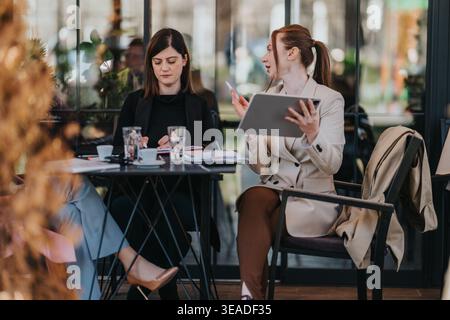 Zwei professionelle Frauen bei einem Geschäftstreffen in einem Café im Freien, um Dokumente und ein Tablet zu diskutieren Stockfoto