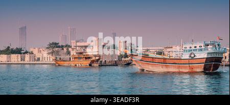 12. Januar 2026, Dubai, VAE: Traditionelles Dhow-Boot, das auf Creek segelt und das Bur Dubai Heritage Area mit Windtürmen und fernen modernen Skyline zeigt Stockfoto