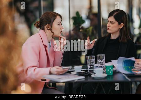 Zwei weibliche Kollegen, die ein ernsthaftes geschäftliches Gespräch über Dokumente und Kaffee in einem Café führen Stockfoto