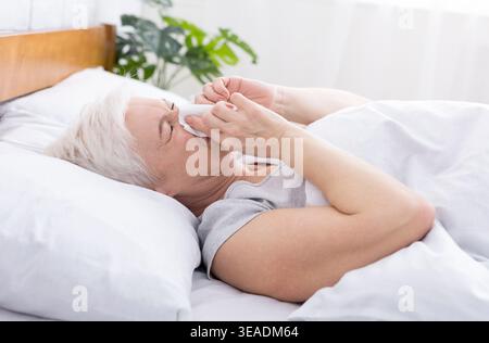 Ältere Frau, die die Nase mit Gewebe bedeckt, während sie zu Hause niest Stockfoto