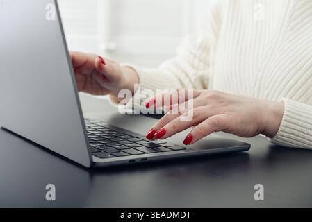 Nahaufnahme weiblicher Hände mit roter Maniküre auf einer Laptop-Tastatur. Konzept von Fernarbeit, Online-Kommunikation, digitalen Diensten und modernen LIFE Stockfoto