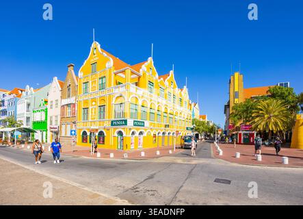 Ikonisches gelbes Penha-Gebäude mit niederländischer Kolonialarchitektur in einer sonnigen Straße mit Menschen in Willemstad Curacao Stockfoto