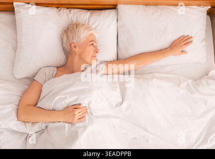 Entspannte Frau im Bett mit weißem Bett in gemütlicher Schlafzimmerumgebung Stockfoto