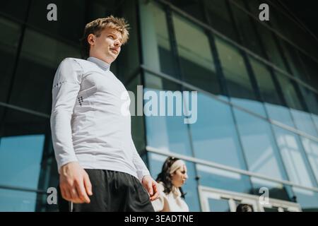 Junge Sportler in Sportbekleidung, die an einem sonnigen Tag vor einem modernen Glasgebäude spazieren Stockfoto