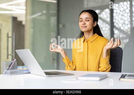 Junge Geschäftsfrau findet innere Ruhe und Balance durch Meditation in einem modernen Büroarbeitsplatz, übt Achtsamkeit für geistiges Wohlbefinden und Stressabbau während des arbeitsreichen Arbeitstages Stockfoto