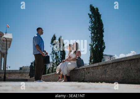 Zwangloses Geschäftstreffen im Freien mit einem Mann, der steht und zwei Frauen auf einer niedrigen Steinmauer sitzen Stockfoto