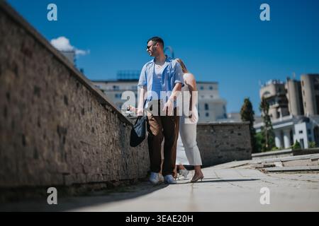 Zwangloses Paar spazieren in einer sonnigen Stadt in der Nähe von Bürogebäuden für Reise- und Geschäftskonzepte Stockfoto