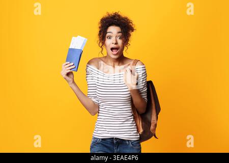 Begeisterte Reisende mit Tickets und Rucksack mit hellgelbem Hintergrund Stockfoto