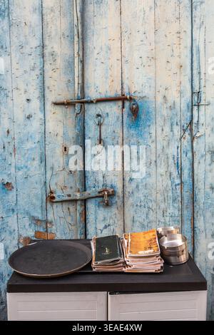 Auf einem Möbelstück vor einer alten, blau getünchten Holztür stehen ein Serviertablett und ein Stapel Speisekarten für die Gäste eines Restaurants Stockfoto