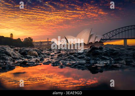 Vom Mrs. Macquarie’s Chair aus leuchtet das Licht des Sonnenuntergangs über dem Opernhaus von Sydney und der Harbour Bridge und reflektiert warme Farben an der Hafenküste. Stockfoto