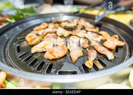 Brutzelnde Speckstreifen, die auf einem koreanischen BBQ-Grill mit verkohlten Kanten und herzhaftem Rauch gegrillt werden, Nahaufnahme Stockfoto