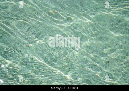 Klares, flaches Wasser, das über den Sandboden plätschert und strukturierte Lichtmuster und Wellenlinien in der natürlichen aquatischen Umgebung erzeugt Stockfoto