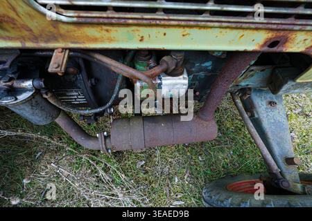 Verrostete Traktormotorkomponenten und Auspuffanlage, die auf einer alten Landmaschine im Freien auf einem Grasfeld abgestellt sind. Stockfoto