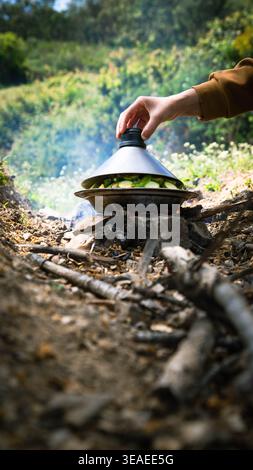 Händeheben eines Tagine-Deckels, Kochen über einem Holzfeuer, sichtbares Gemüse, ländliche Atmosphäre im Freien in der Natur in der Nähe von Tetouan. Stockfoto