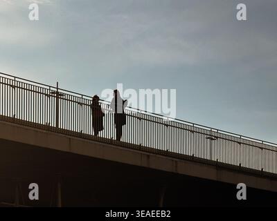 Zwei nicht erkennbare Menschen stehen zusammen auf einer Brücke vor einem weiten offenen Himmel und zeigen Verbindung, Freiheit und Outdoor-Lifestyle Stockfoto