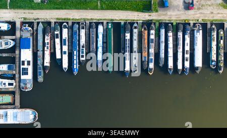 Aus der Vogelperspektive sehen Sie farbenfrohe Schmalboote und Kanalkähne, die an einem Yachthafen mit ruhigem Wasser und einer grasbewachsenen Rawcliffe Bridge, England, Großbritannien, ankern. Stockfoto