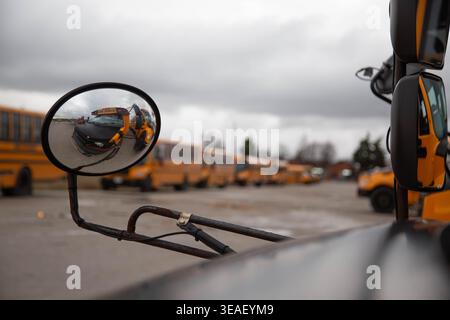 Nahaufnahme eines Seitenspiegels eines Schulbusses, der eine Reihe gelber Busse in einem Depot mit geringer Schärfentiefe reflektiert. Stockfoto