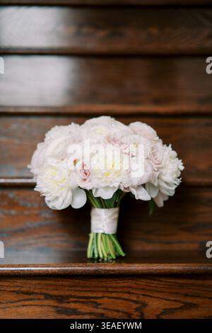 Elegante rosa und weiße Pfingstrosen auf Holzsitz. Handgefertigtes Blumendesign mit strukturierten Stielen und weichen Blütenblättern Stockfoto