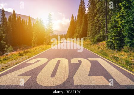 Malerische Straße durch den Wald mit einer hellen Sonne und dem Jahr 2027 gemalt auf dem Bürgersteig. Leere Asphaltstraße und Neujahrskonzept 2027. Fahren auf einem Stockfoto