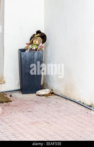 Vogelscheuchen-Puppe im Metallübertopf gegen weiße Wandecke – rustikaler dekorativer Garten-Akzent Stockfoto
