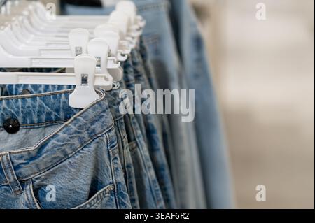 Reihen blauer Jeans hängen an weißen Kunststoffbügeln in einer modernen Boutique. Selektiver Fokus auf Denim-Textur und -Taschen. Modeeinzelhandel Stockfoto