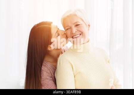 Junge Frau, die ältere Mutter auf die Wange küsst Stockfoto