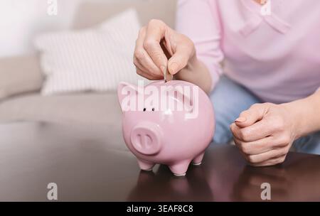 Alte weibliche Hand, die Münzen in rosafarbene Schweinebank steckt Stockfoto