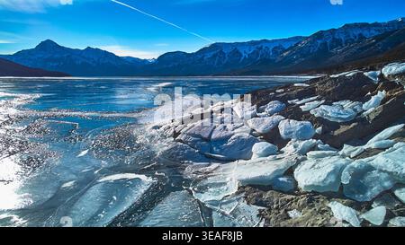 Frozen Lake Ice Sheets Rocky Shore und Snow Capped Mountains im Winter Sonnenlicht Stockfoto