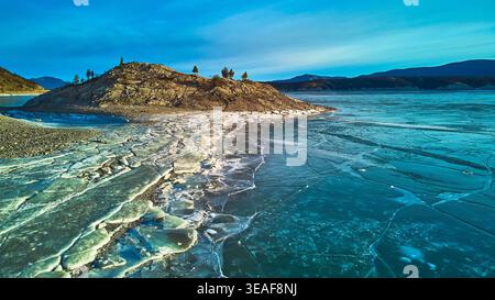 Luftgefrorener See mit Cracked Ice und Rocky Island in der Winterlandschaft Stockfoto