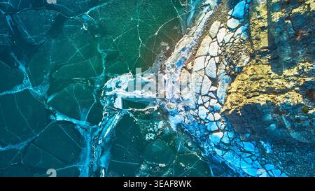 Aerial Frozen Lake Cracked Ice Patterns und Rocky Shoreline Winter Top Down Stockfoto