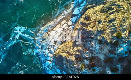 Aerial Frozen Lake Cracked Ice und Rocky Shoreline Top Down Winter Perspektive Stockfoto