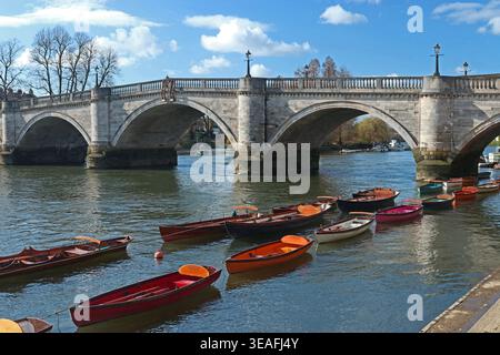 Richmond upon Thames, London. Farbenfrohe Ruderboote zum Verleih vertäut im Vordergrund, Richmond Bridge Hintergrund. Blauer Himmel, warmer sonniger Tag im März Stockfoto