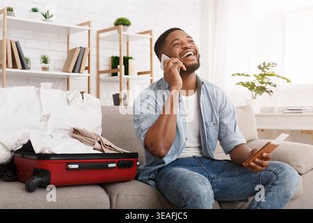 Happy african-american man Vorbereitung auf Reisen, am Telefon sprechen Stockfoto