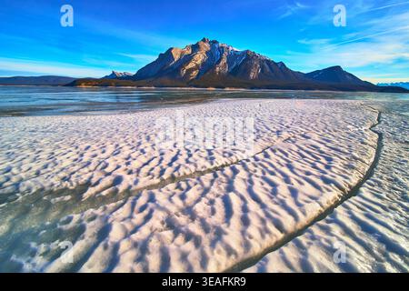 Frozen Lake Ice Patterns und Snowy Mountain Peaks unter dem blauen Winterhimmel Stockfoto