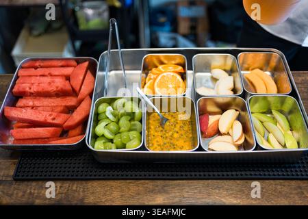 Auswahl an bunten geschnittenen Früchten, darunter Wassermelone, Orange, Trauben, Passionsfrucht, Melonen- und Kantaloupe-Früchte, die in einem Metallbehälter am Bar-Set belegt werden Stockfoto