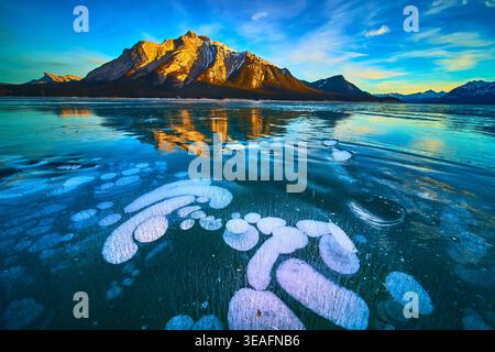 Gefrorene Lake Ice Bubbles und majestätische Snowy Mountains im lebhaften Winteruntergang Stockfoto