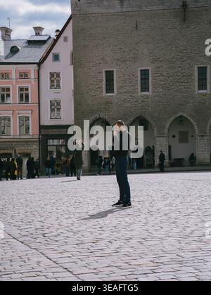 Mann auf dem Kopfsteinpflasterplatz in der Altstadt von Tallinn, Estland, mit mittelalterlichen Gebäuden und Touristen im Frühling Stockfoto