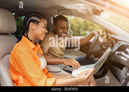 Das junge Schwarze Paar lächelt, während er zusammen im Auto auf die Papierkarte blickt Stockfoto